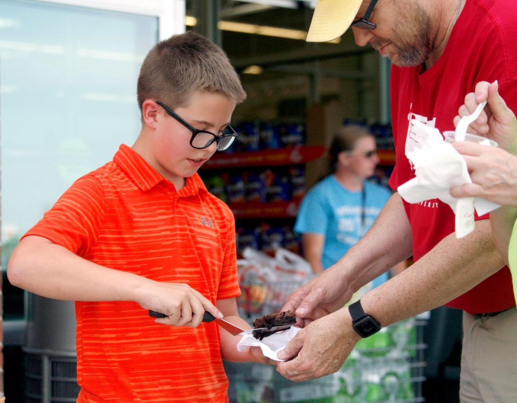Tate Brown, 12, of Kearney, left, scoops out a brownie for a customer Friday evening during the Biz Kidz Camp product showcase at the Kearney Hy-Vee. (Photo by Tyler Ellyson, UNK Communications)
