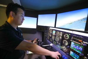 Jaehyun Kim, who graduated last week with a bachelor’s degree in aviation systems management, demonstrates the Redbird flight simulator inside UNK’s Otto C. Olsen building. The simulator allows aviation students to practice flying in different environments and it’s an important tool when they’re learning how to handle emergency situations. (Photo by Corbey R. Dorsey, UNK Communications)