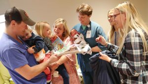 Jamie Cummings, a registered nurse at Kearney Regional Medical Center, holds newborn Titus Vest as members of the Vest family, from left, Talus, 2-year-old Haven, 5-year-old Estelle and Caitlin, receive gifts from UNK students Shyenne Cooper of North Platte, front right, and Gussie Rhoades of Giltner. Students in professor Jeanne Stolzer’s child and adolescent development class delivered presents to hospital patients Wednesday as part of a service project. (Photo by Corbey R. Dorsey, UNK Communications)
