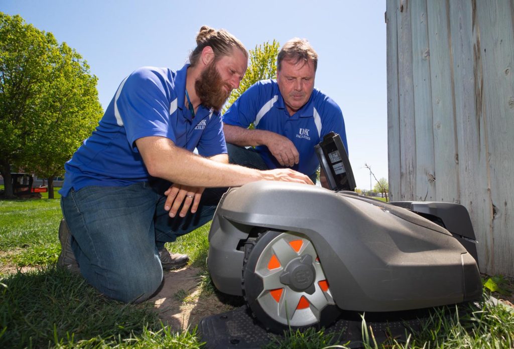 Michael Sup, left, and Dick Wardyn with UNK Facilities Management and Planning set up a robotic mower at its charging station on campus. UNK owns two Husqvarna Automowers that maintain the marching band practice field between the College of Education building and West Center. (Photo by Corbey R. Dorsey, UNK Communications)