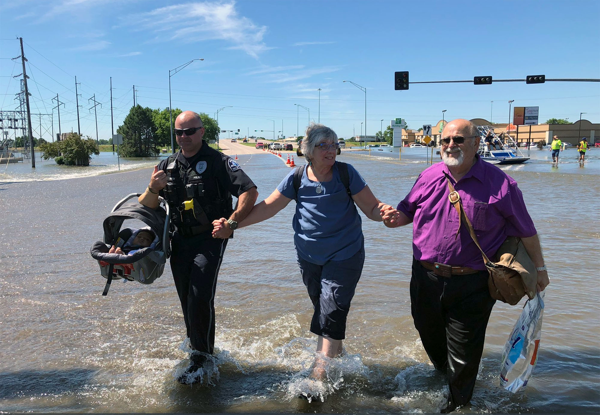 Kearney Police Officer Derek Payton assists Leslye and Terry Taylor of Pueblo, Colorado, and their 3-month-old grandson as they walk through the floodwater Tuesday after evacuating a local hotel. (Photo courtesy of Kearney Police Department)