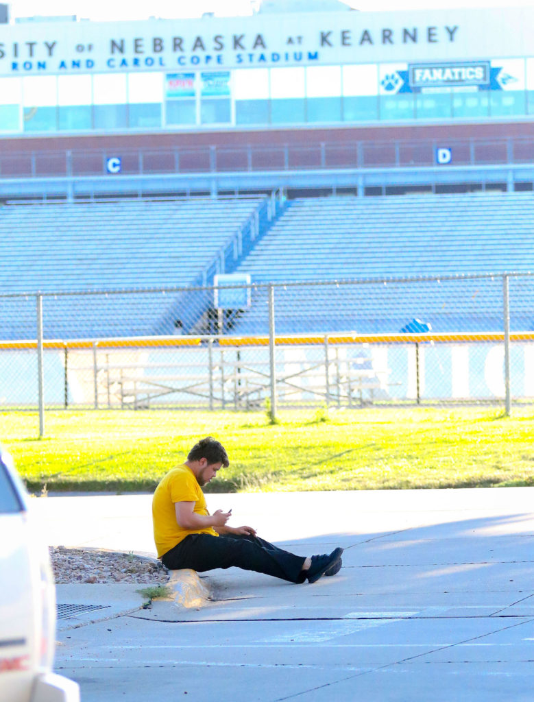 Robert Hubley watches videos on his phone while relaxing Wednesday evening in the parking lot of Centennial Towers West at UNK. Hubley moved from Oklahoma to Kearney one month ago, got married Sunday and moved into temporary housing at UNK after flooding forced him to evacuate his cousin’s home. (Photo by Todd Gottula, UNK Communications)