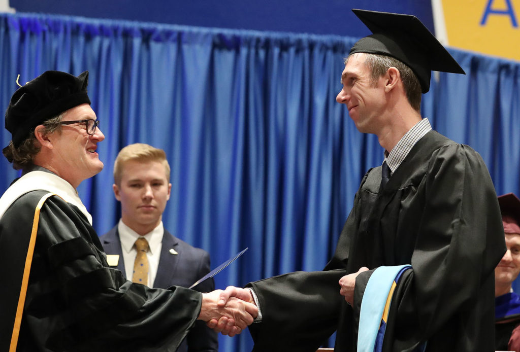 UNK Dean of Graduate Studies Mark Ellis, left, congratulates Brett Kluever during Friday’s winter commencement at the Health and Sports Center. Kluever and his wife Sara both received Master of Education degrees in instructional technology.