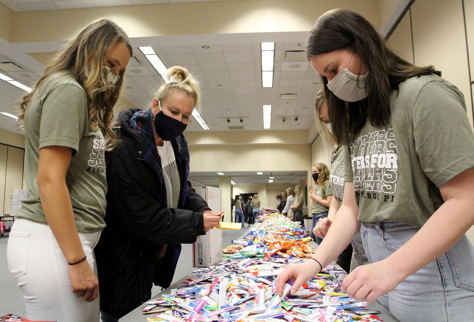 Alpha Omicron Pi members Jessie Daake of Kearney, left, and Ashley Sweet of North Platte, right, help Daake’s mother Lynda create a care package for a U.S. military member during Tuesday evening’s Sisters for Soldiers event.