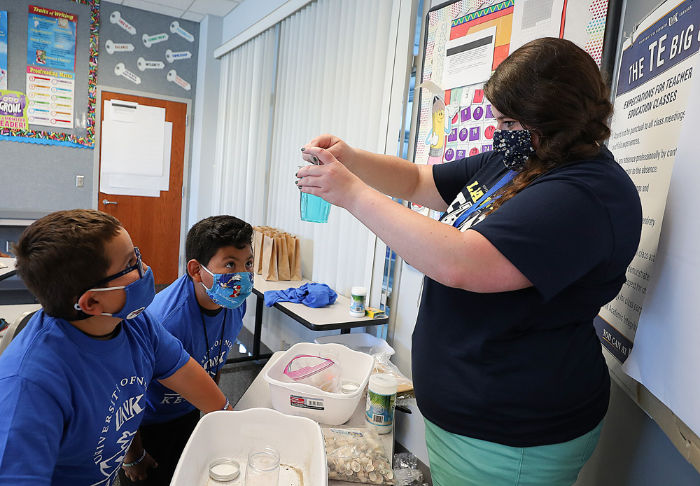 PAWS University teacher Braelyn Verba, right, mixes blue coloring in a jar to help Kruz Granados, left, and DaRey Aldaba Montanez create an ocean scene during the “Disney Designers” PAWS University workshop at UNK. (Photos by Erika Pritchard, UNK Communications)