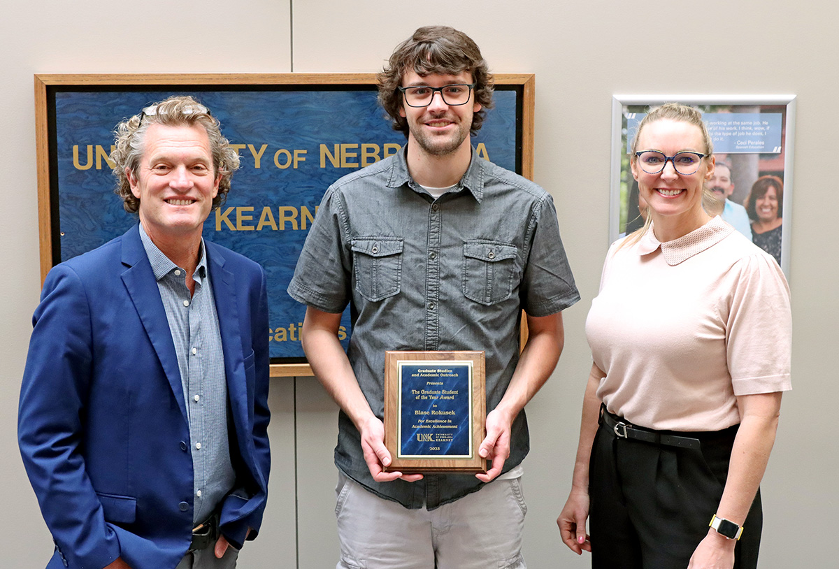 Blase Rokusek, center, receives the UNK Graduate Student of the Year Award from Dean of Graduate Studies and Academic Outreach Mark Ellis and Associate Dean Megan Adkins.