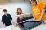 Professor Victoria Goro-Rapoport, left, and University of Nebraska at Kearney student Lim Yun Ji of Korea, right, work with Morgan Boldt of Amherst on a printmaking project Wednesday at UNK’s Imagination Day. (Photo by Corbey R. Dorsey, UNK Communications)