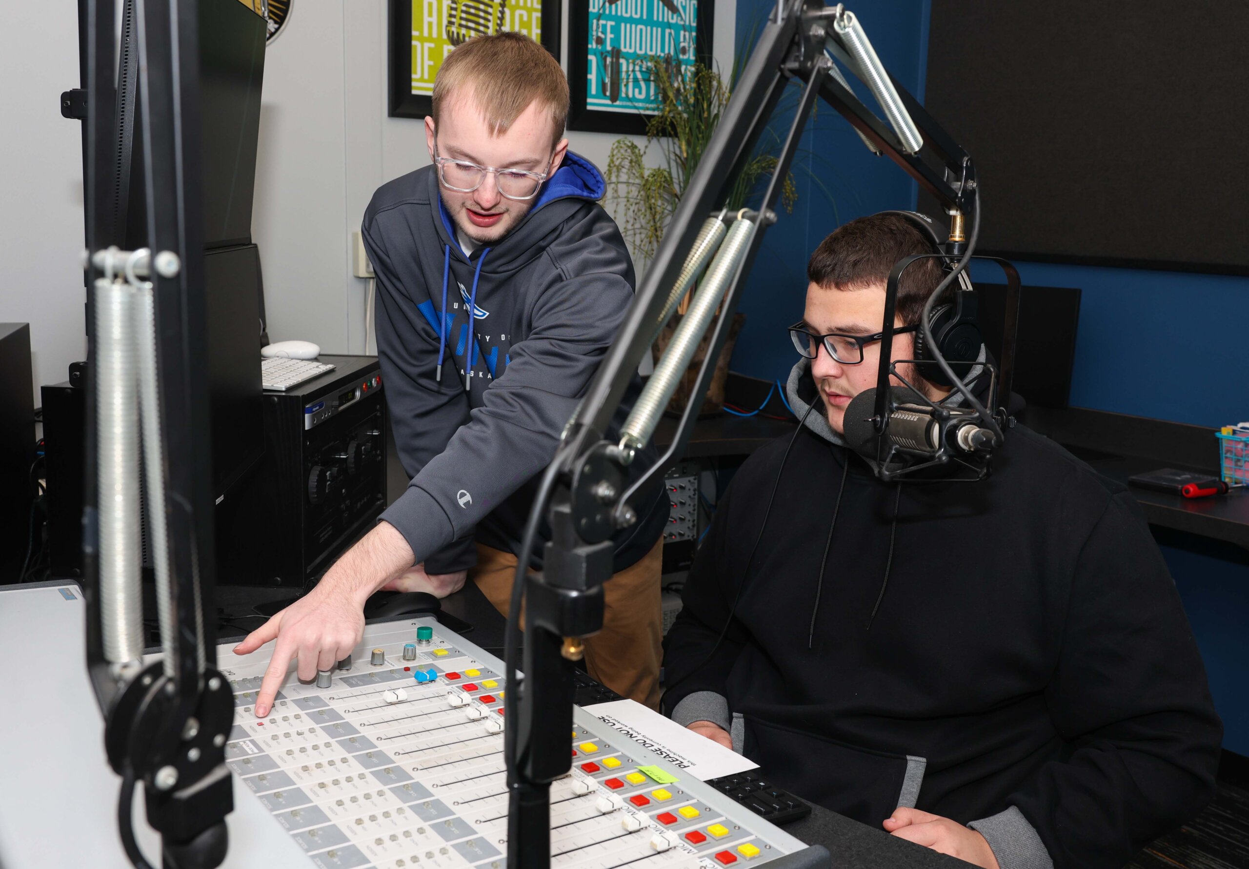 A student shows his peer how to operate the control panel at the student radio station.