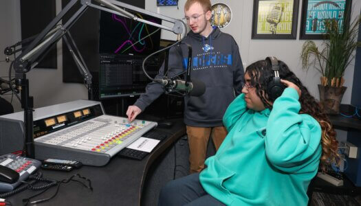 A student teaches his peer about the student radio station.