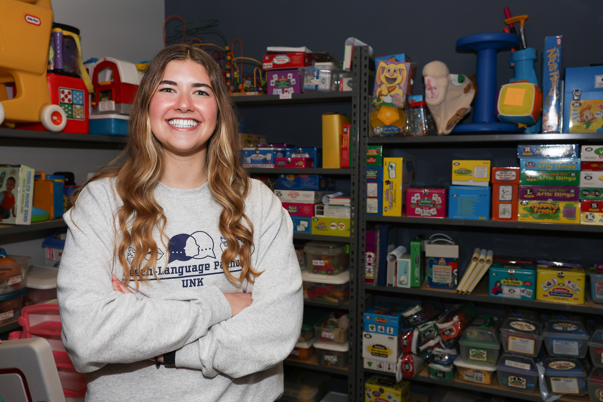 Kylie Baumert poses for a photo, surrounded by toys and games used for pediatric speech therapy.