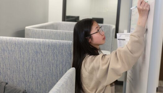 A student writes on a whiteboard in the library.