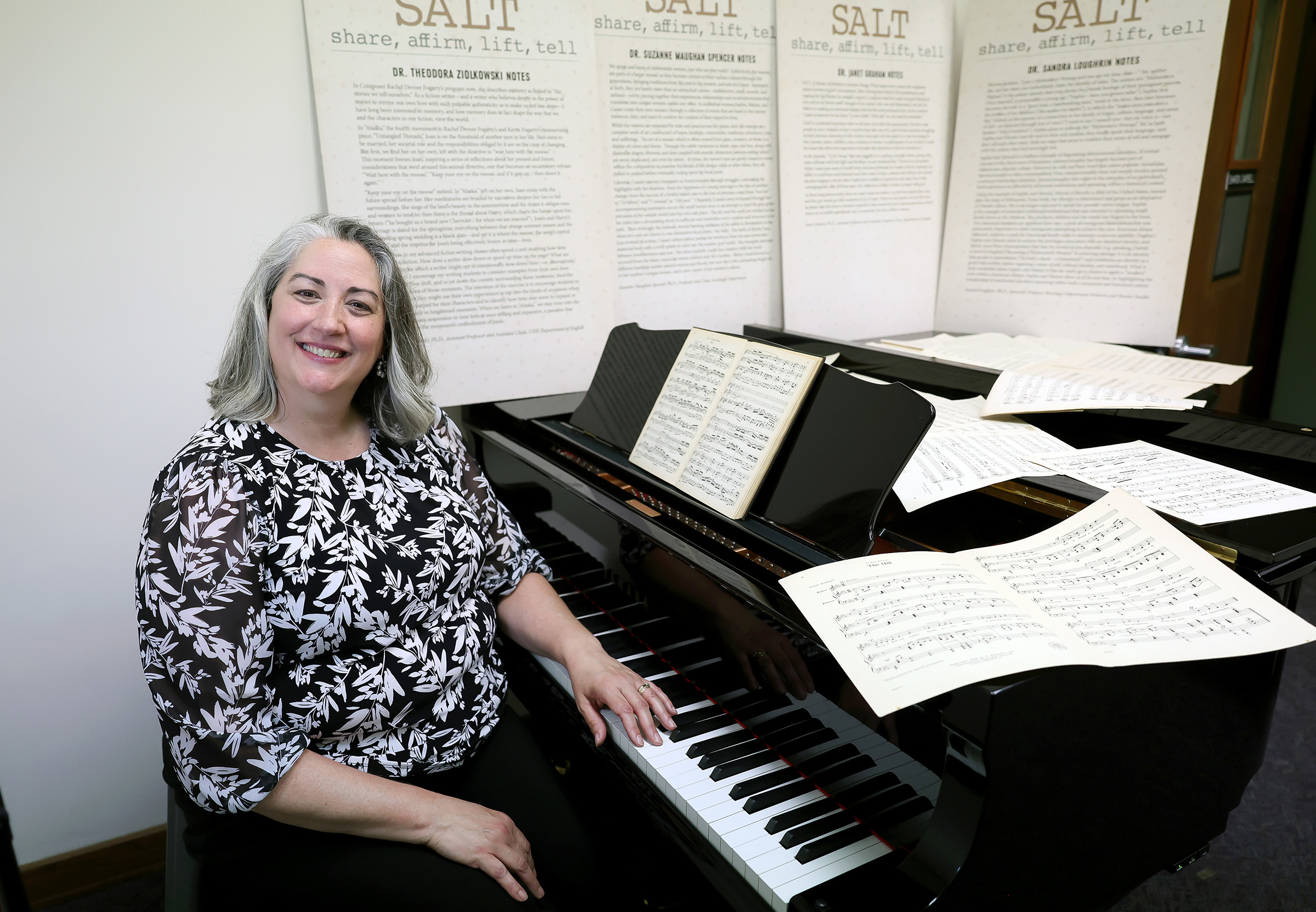 UNK music professor Sharon Campbell is pictured seated at a piano with sheet music.