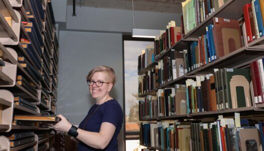 A woman smiles at the camera while holding a book in the archive room.