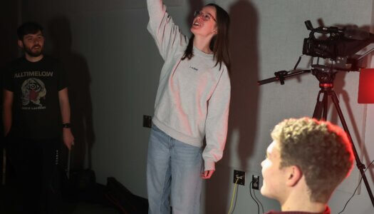 A student adjusts a studio light facing another student.