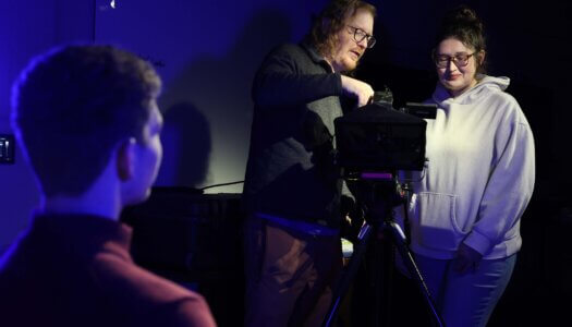 A professor shows a student how to operate a video camera.