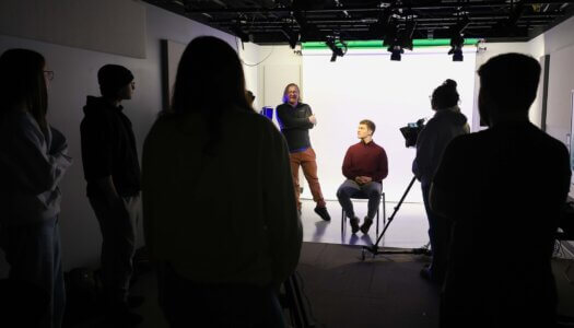 Students listen to a professor in a video studio.