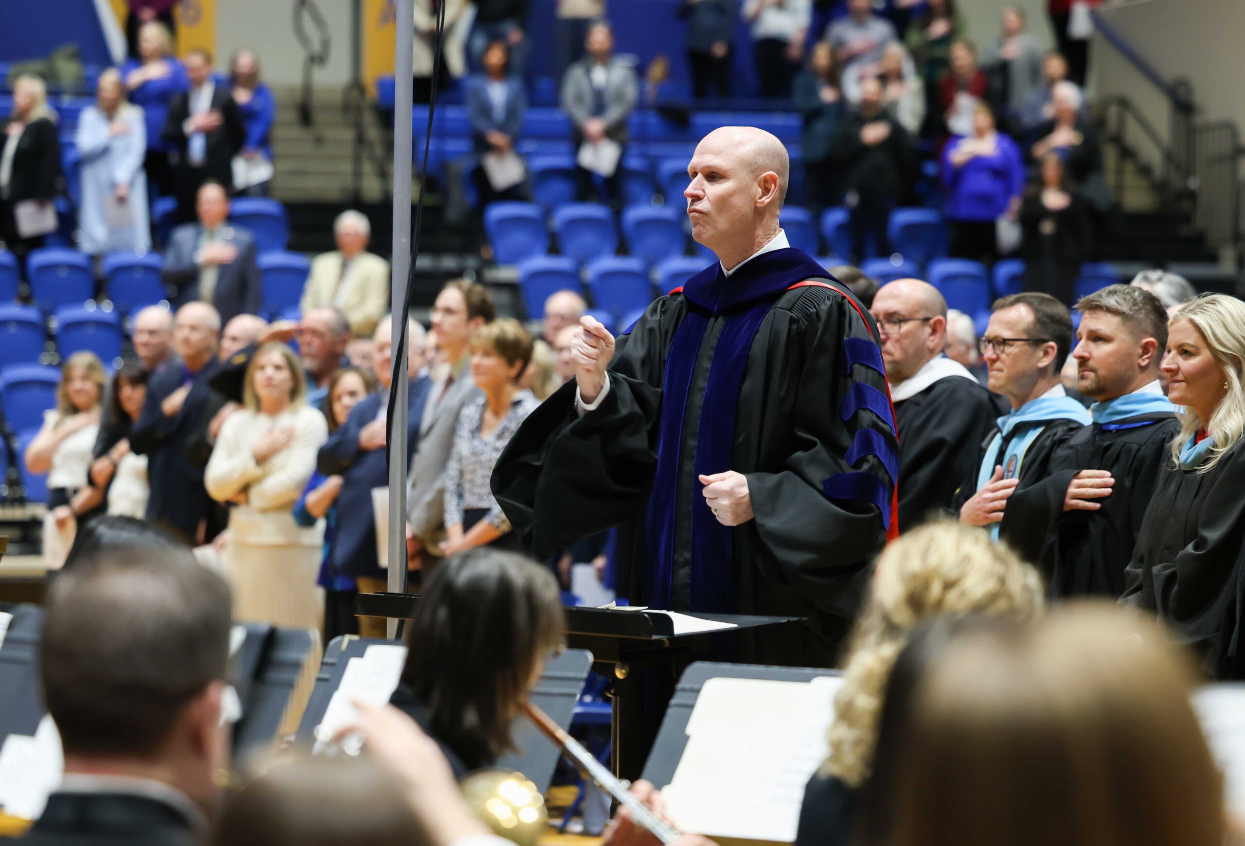 Chancellor Neal Schnoor leads the UNK Wind Ensemble during the national anthem at Friday's investiture ceremony.