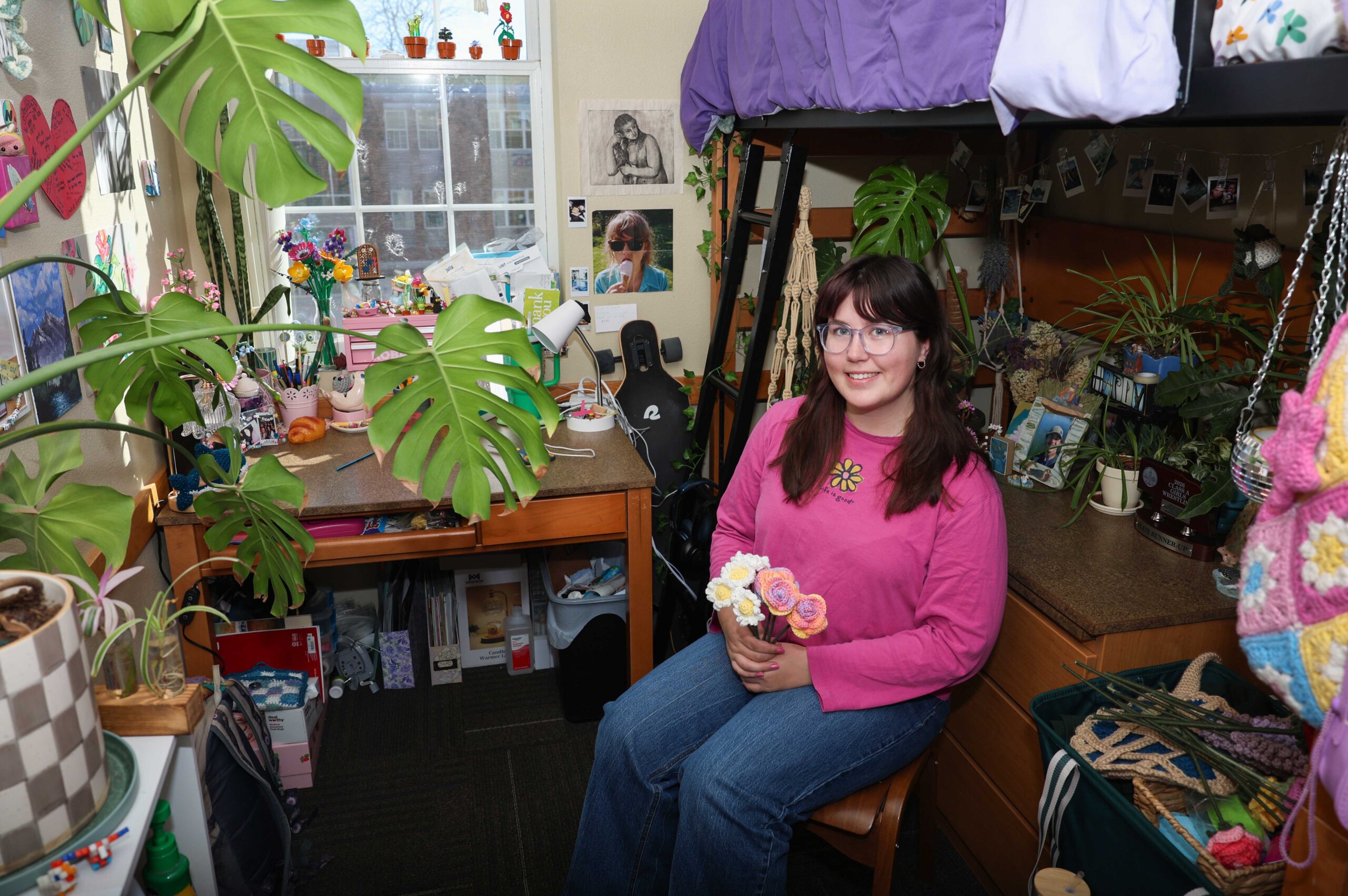 UNK junior Julia McKlem poses for a photo in her residence hall room on campus, surrounded by plants and the crafts she enjoys.