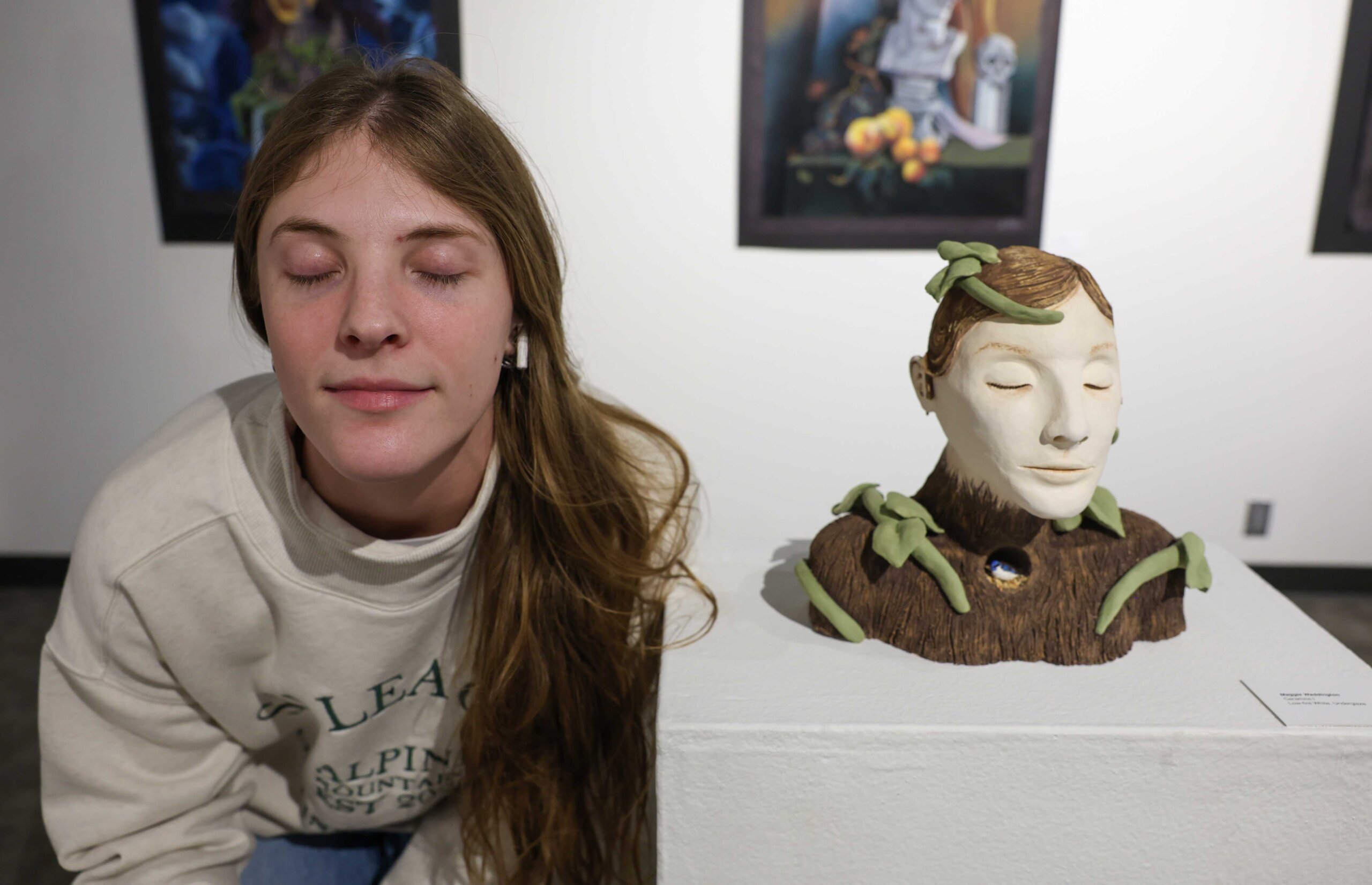 UNK student Maggie Waddington poses next to her self-portrait sculpture with her eyes closed.