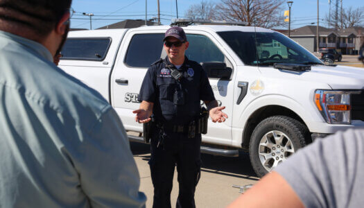 A law enforcement officer talks to students in front of his vehicle.