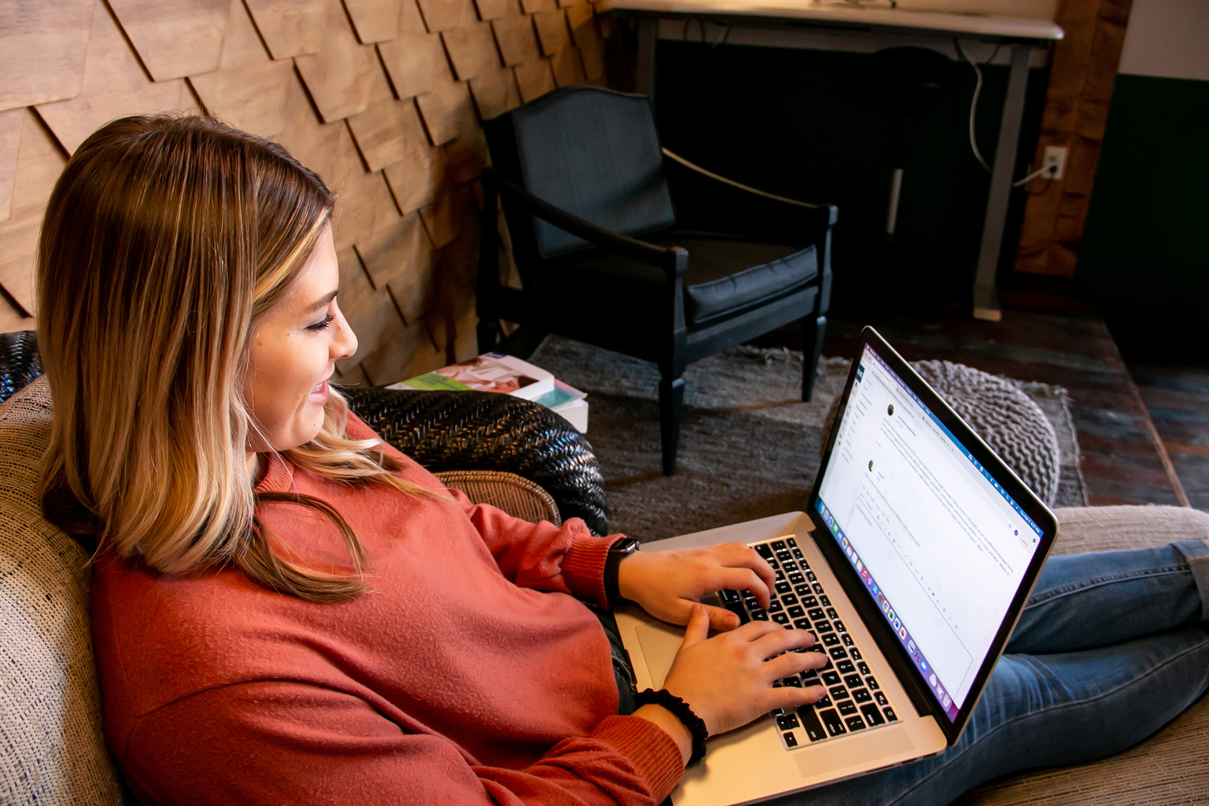 A UNK student relaxes in a chair while working on her laptop.