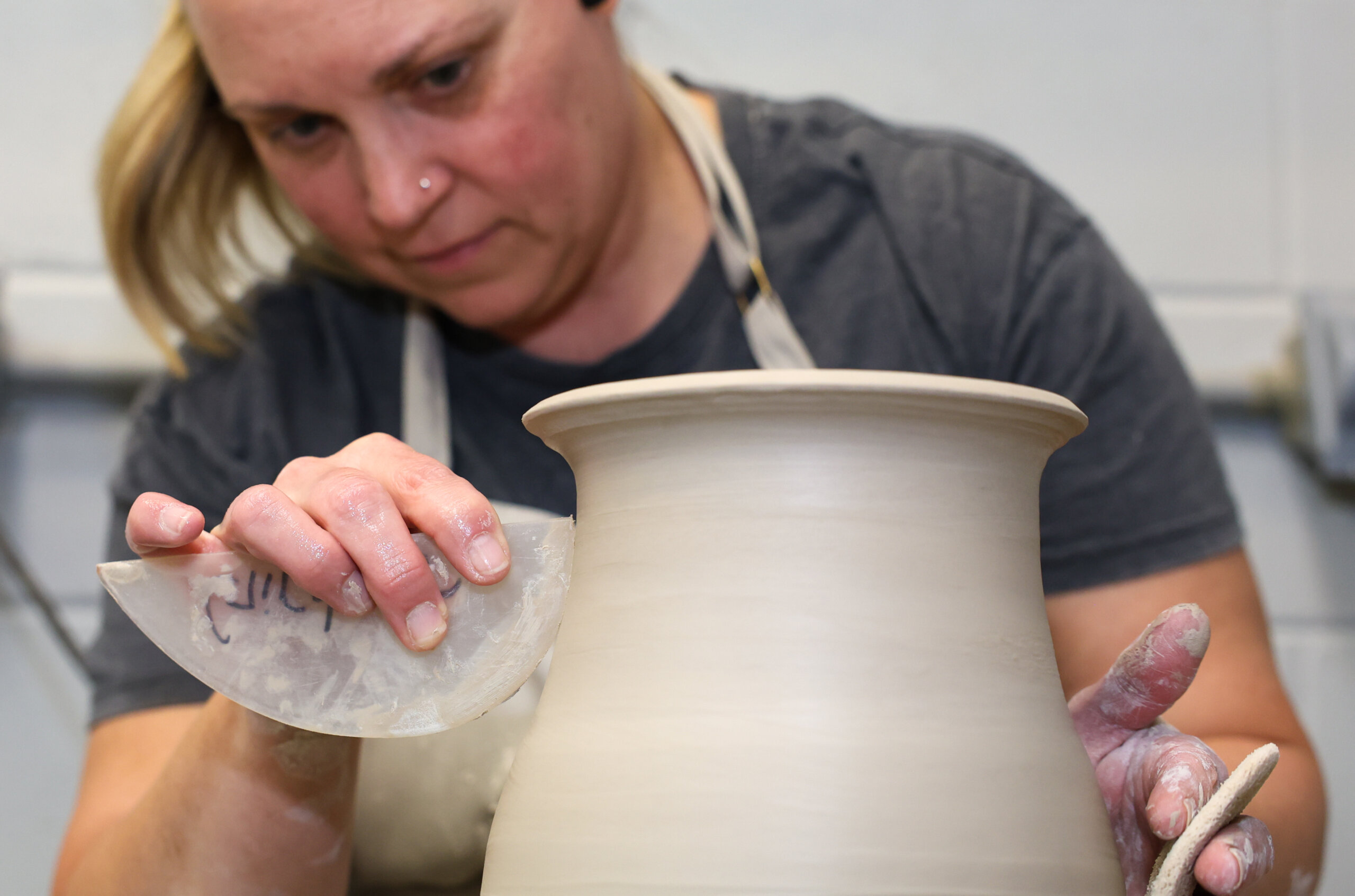 A woman shapes a pot on a wheel.