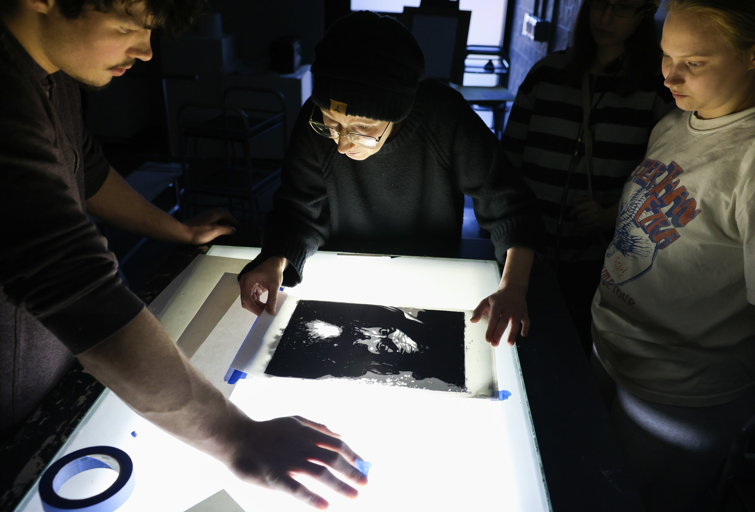 People stand around a light table with a print.