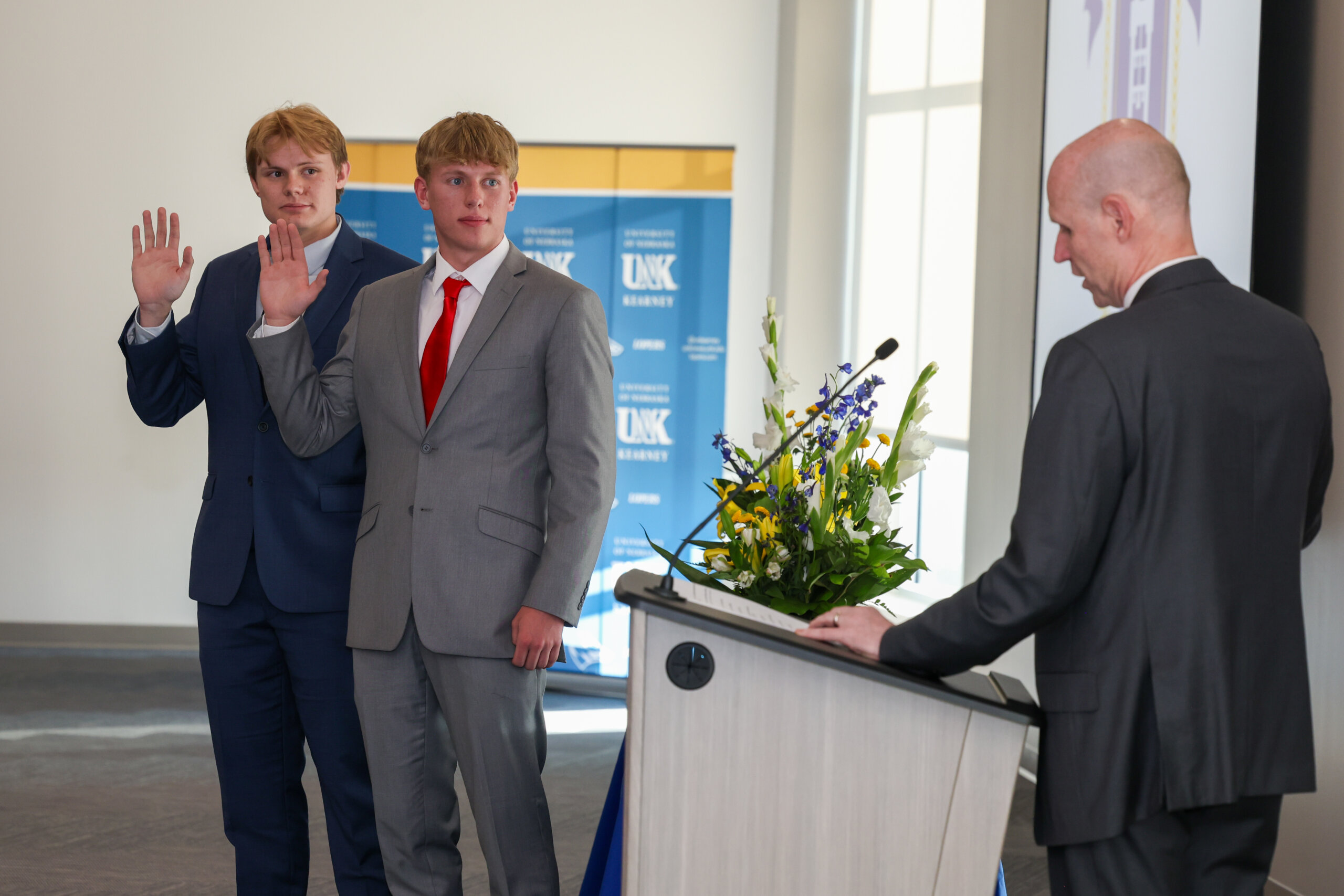 Two male students and a man raise their right hands. 