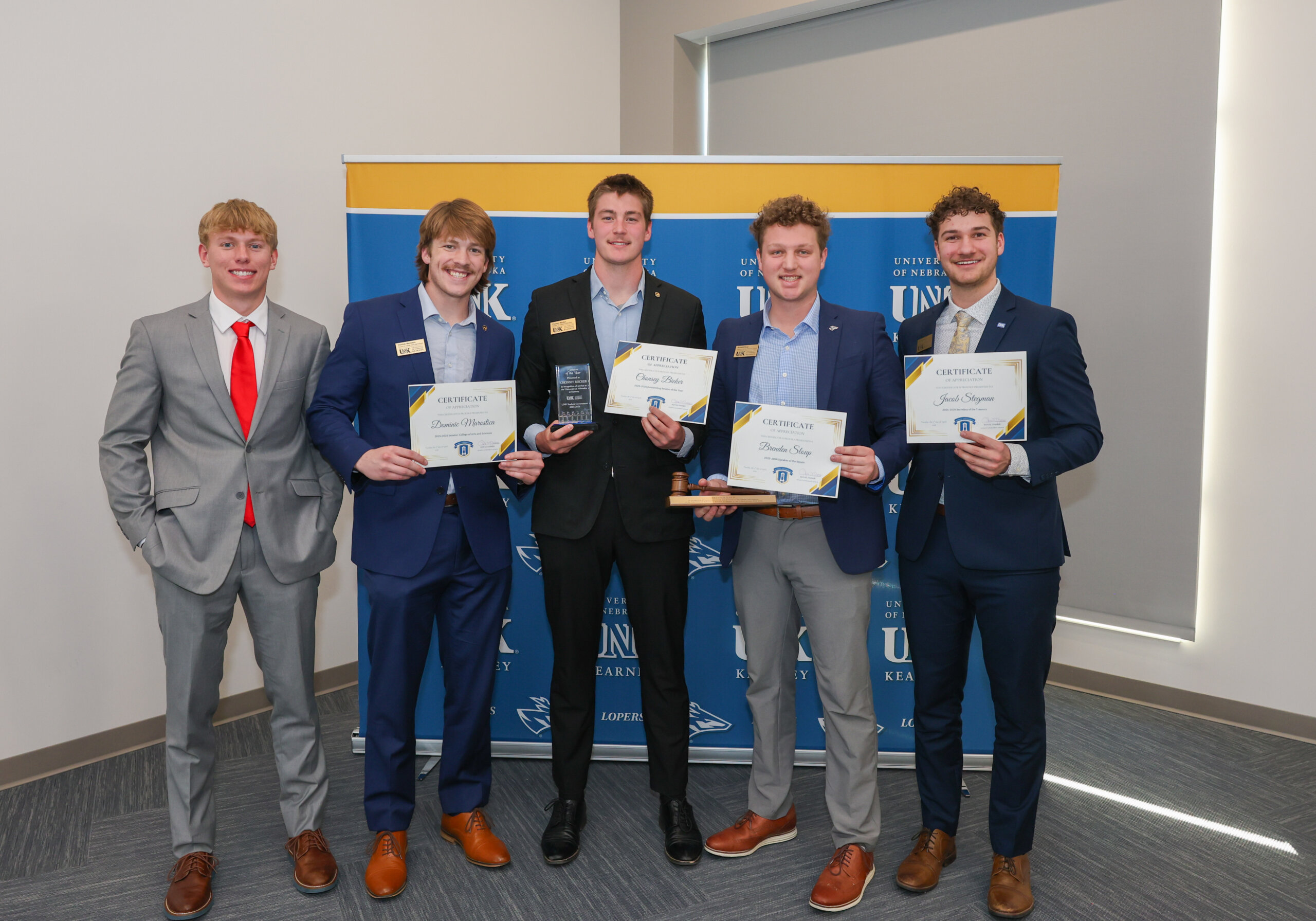 A group of male students hold up certificates.