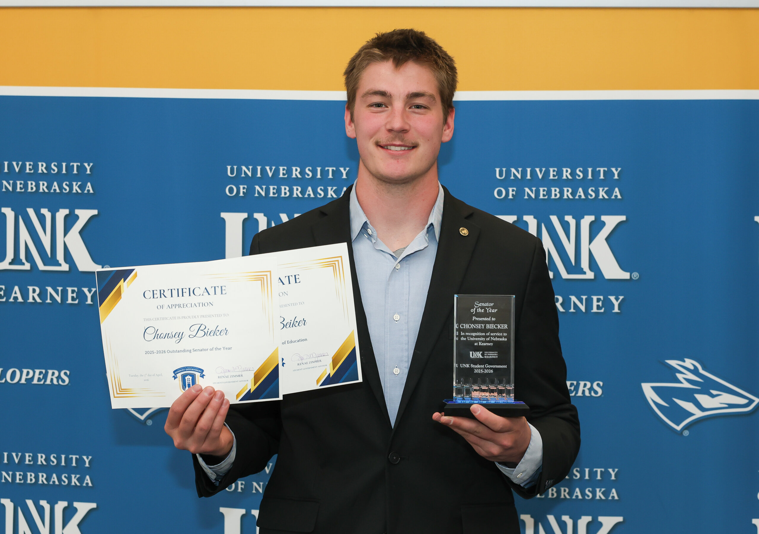 A student holds up certificates and a plaque.