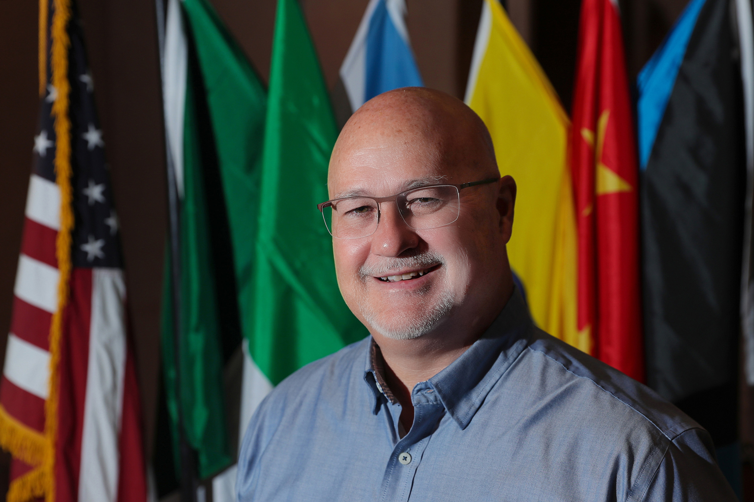 Tim Burkink poses for a photo with flags in the background.