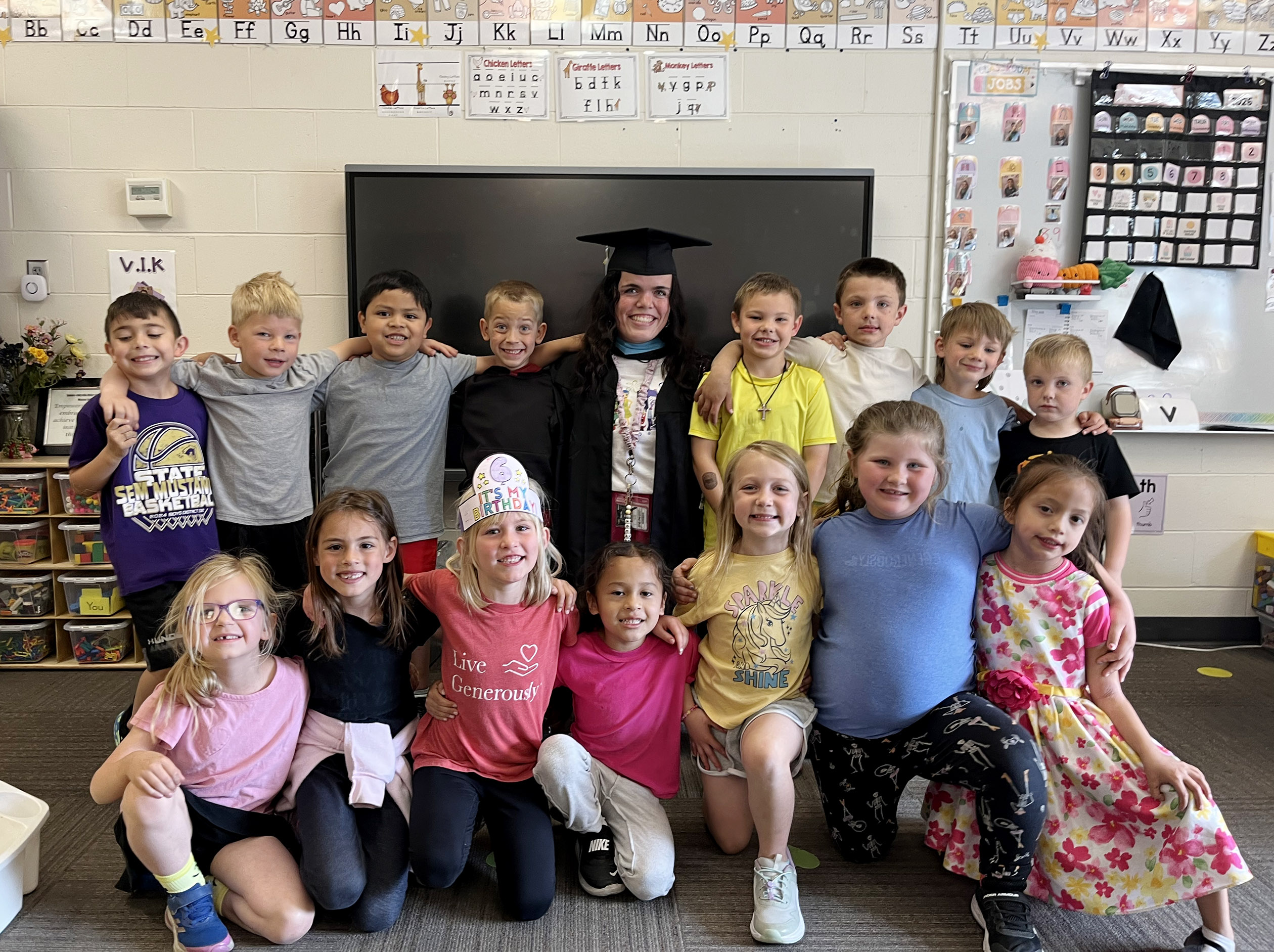 Wearing a graduation cap and gown, Emme Brown poses for a photo with her students.