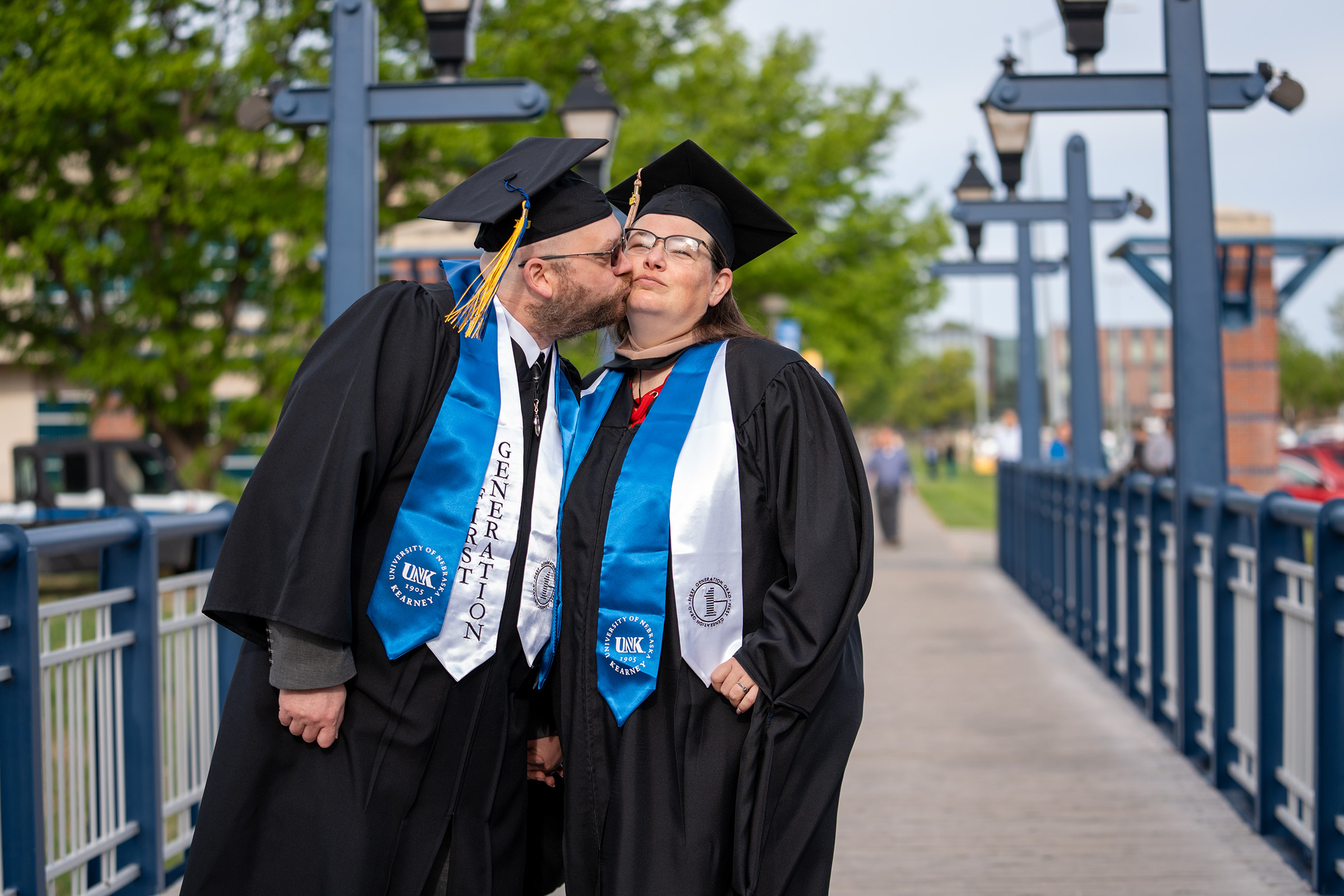 Dressed in their graduation regalia, Matthew Welte kisses his wife Kathy outside UNK's Health and Sports Center.