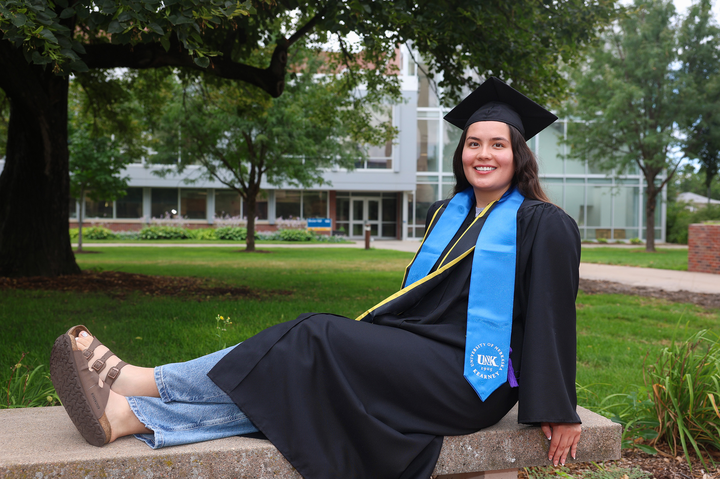 Laura Velasco poses for a photo on the UNK campus in her graduation cap and gown.