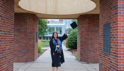 Laura Velasco poses for a photo on the UNK campus in her graduation cap and gown.