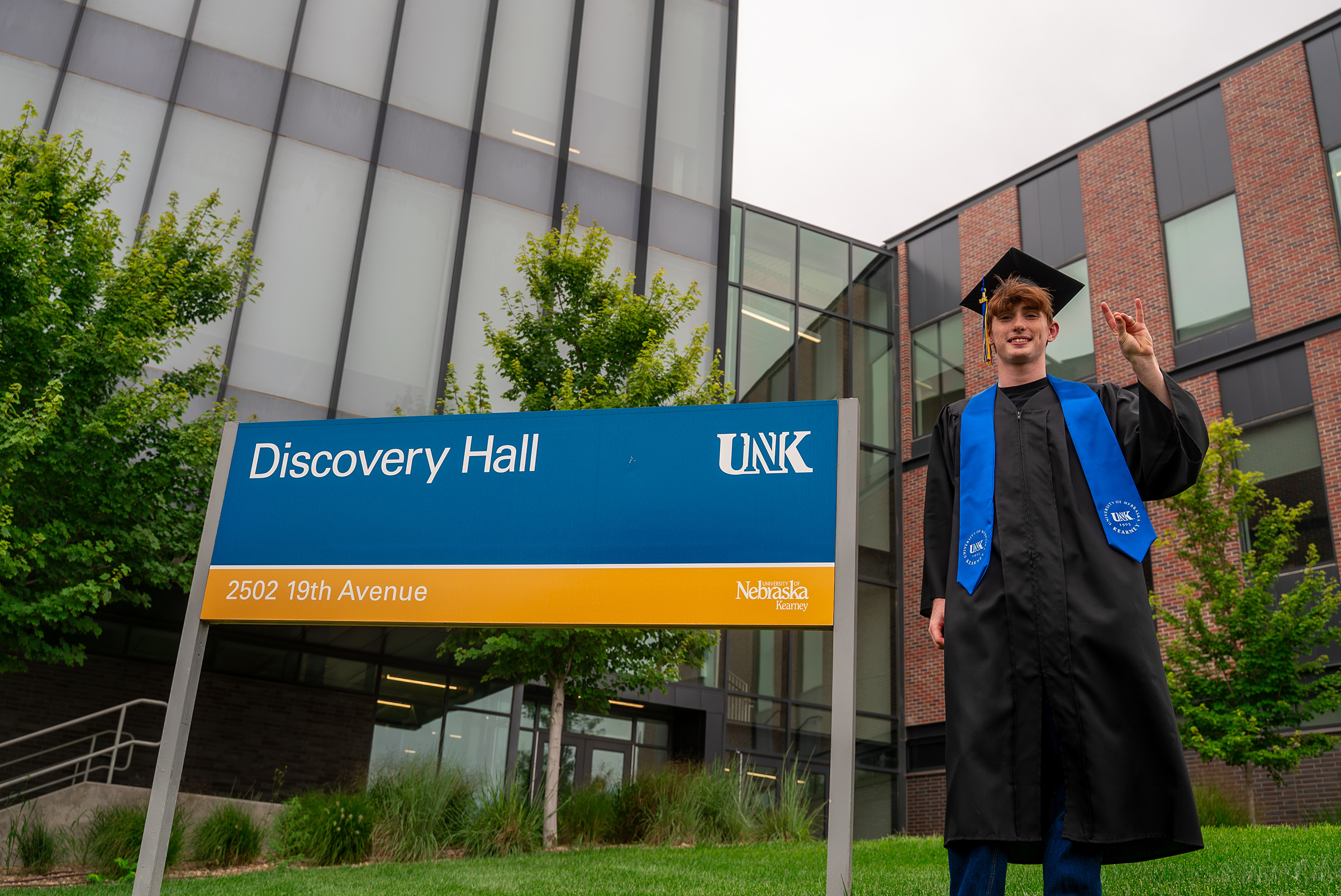 Thomas Safago poses for a photo outside Discovery Hall in his graduation cap and gown.