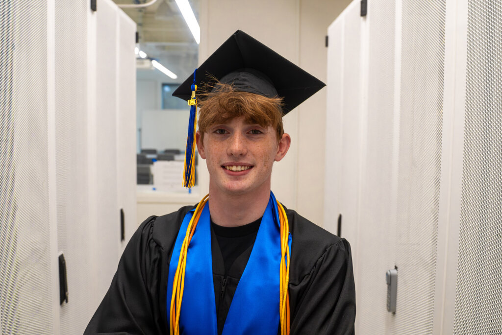 Thomas Safago poses for a photo inside Discovery Hall wearing his graduation cap and gown.