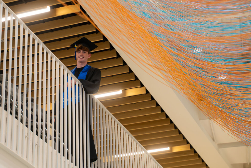 Thomas Safago poses for a photo inside Discovery Hall wearing his graduation cap and gown.