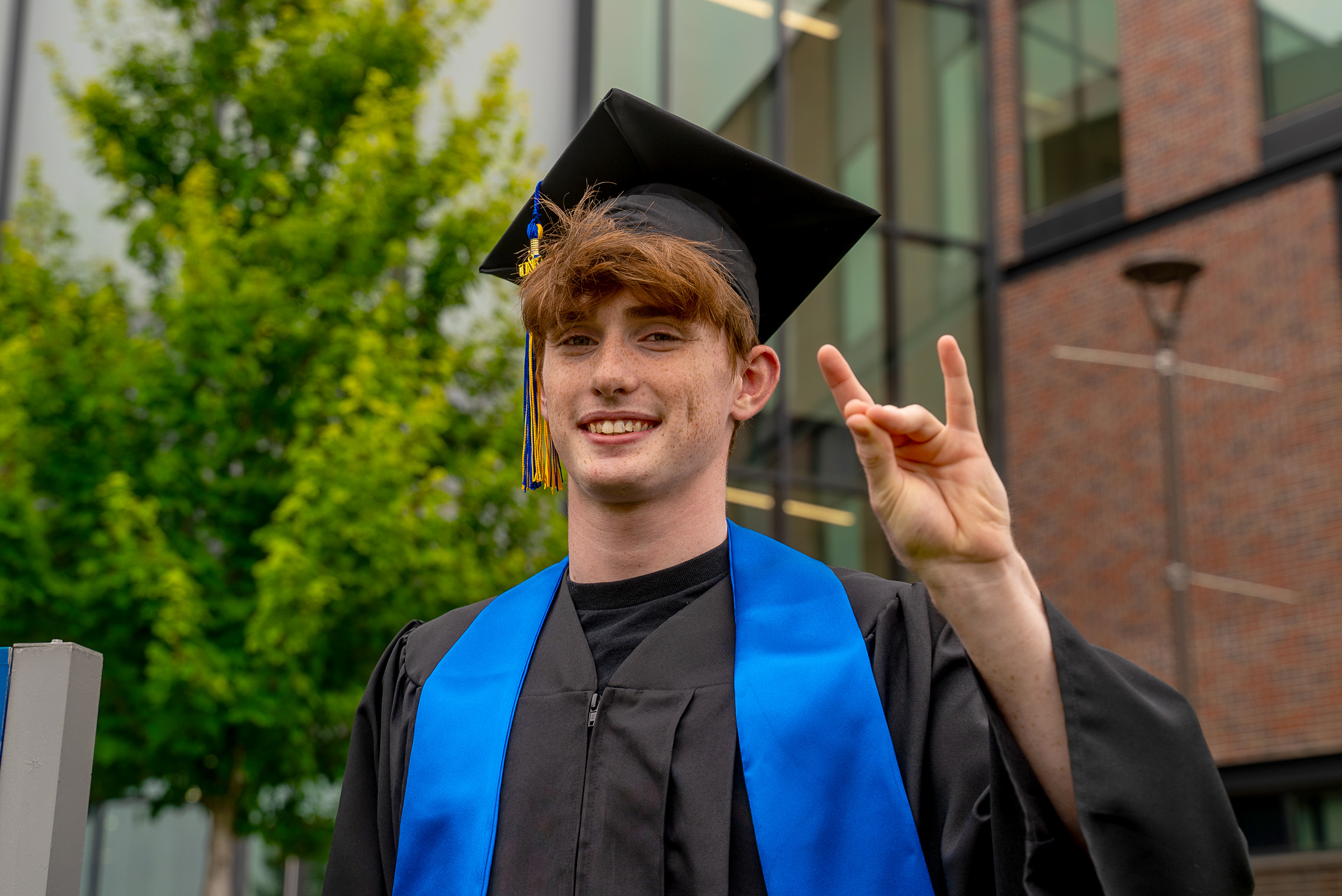 Thomas Safago poses for a photo outside Discovery Hall in his graduation cap and gown.