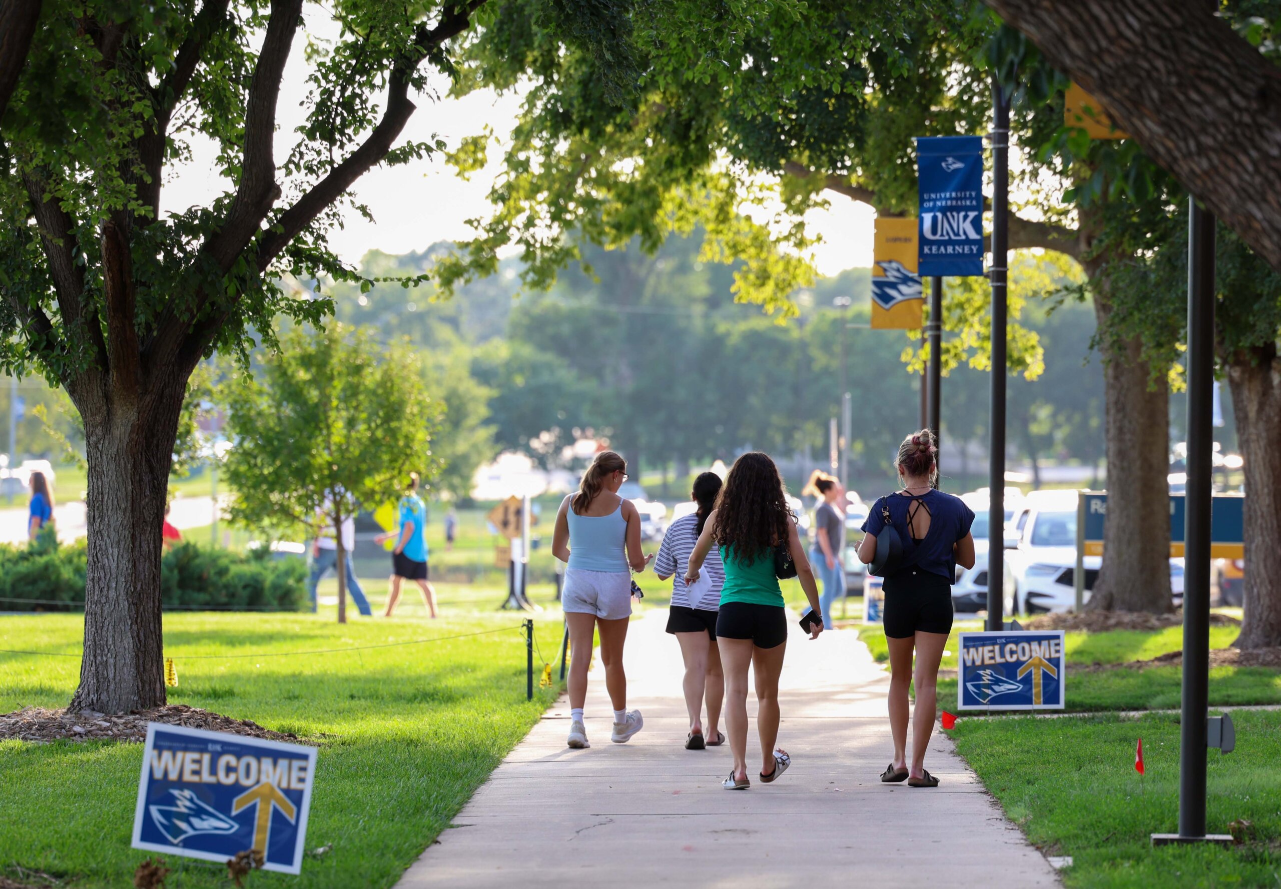 Students walking down the sidewalk next to welcome signs.